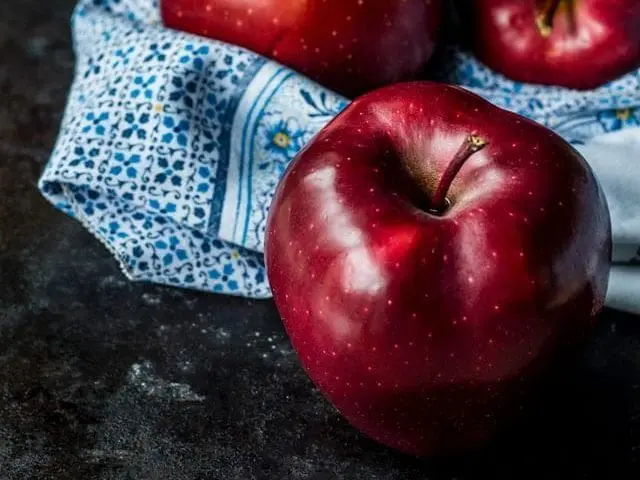 Trzy jabłka, ułożone na białym materiale w granatowe wzory. 