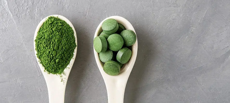 Spirulina, 5 powodów dla których musisz zacząć ją spożywać Drewniana łyżka ze spiruliną w proszku i w kapsułkach.