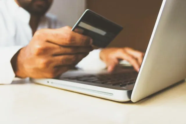 Dłoń z kartą płatniczą przy laptopie, niewyjaśnione wydatki partnera