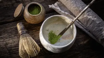 Sproszkowana matcha w czarce i bambusowa miotełka chasen na drewnianym stole