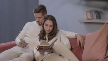 Objawy zdrady: mężczyzna na kanapie wpatrzony w telefon obok partnerki czytającej książkę