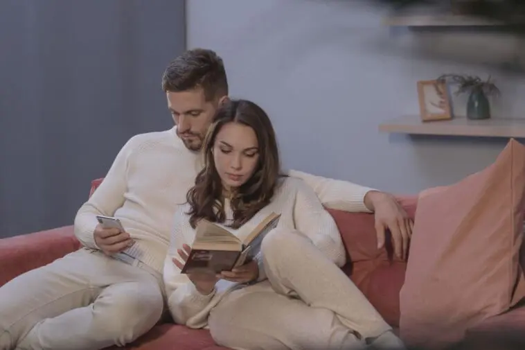 Objawy zdrady: mężczyzna na kanapie wpatrzony w telefon obok partnerki czytającej książkę