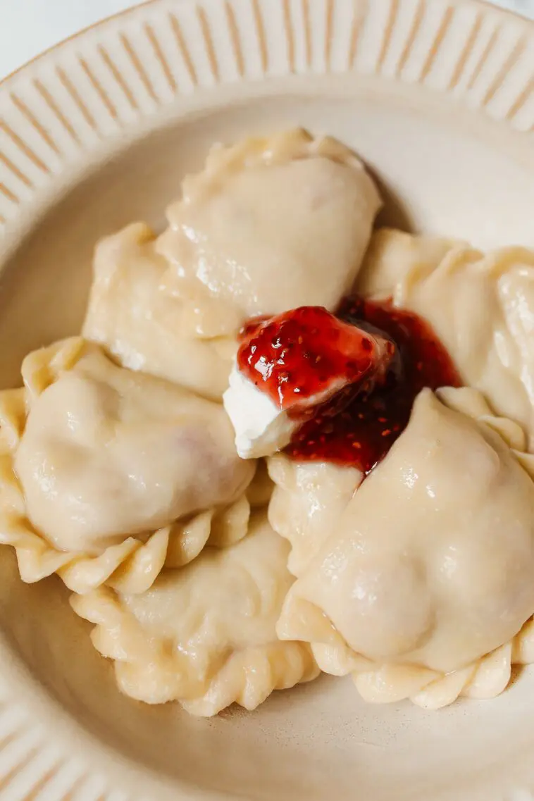 Ciasto na pierogi Magdy Gessler – miękkie, elastyczne i nie pęka Talerz pełen ugotowanych pierogów z okrasą – ciasto na pierogi według przepisu Magdy Gessler