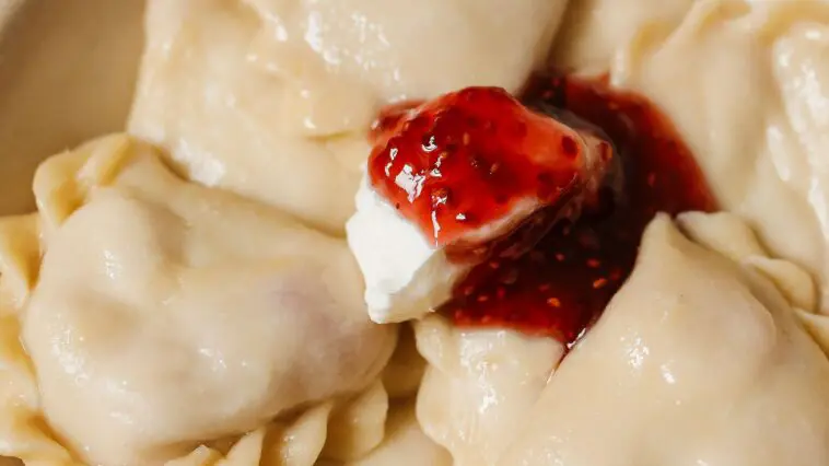 Talerz pełen ugotowanych pierogów z okrasą – ciasto na pierogi według przepisu Magdy Gessler