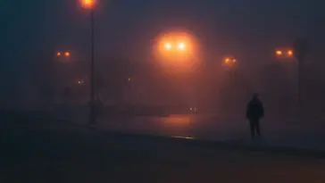 Sylwetka człowieka idącego mglistą ulicą nocą – ilustracja do sennika o strzelaninie