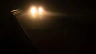 Reflektory samochodu we mgle na mokrej nocnej drodze - ilustracja do artykułu sennik wypadek samochodowy