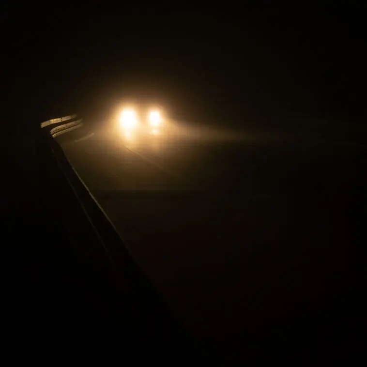 Reflektory samochodu we mgle na mokrej nocnej drodze - ilustracja do artykułu sennik wypadek samochodowy