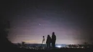 Sylwetki dwóch osób obserwujących rozgwieżdżone nocne niebo podczas roju meteorów