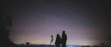 Sylwetki dwóch osób obserwujących rozgwieżdżone nocne niebo podczas roju meteorów