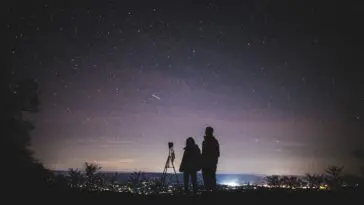 Sylwetki dwóch osób obserwujących rozgwieżdżone nocne niebo podczas roju meteorów