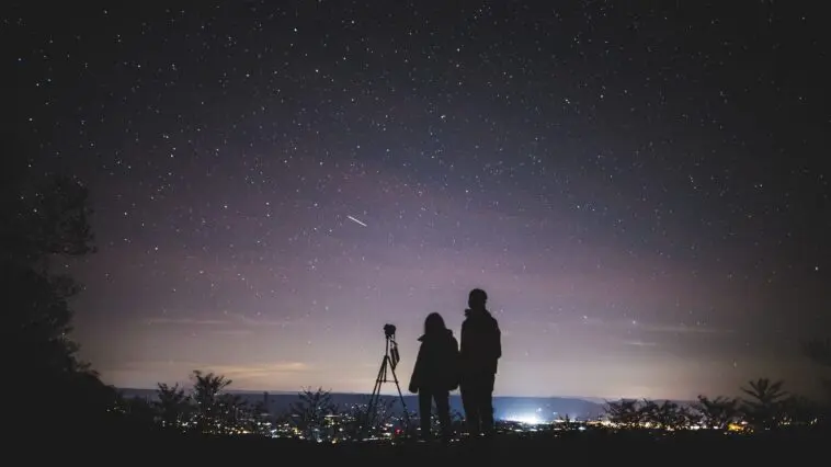 Sylwetki dwóch osób obserwujących rozgwieżdżone nocne niebo podczas roju meteorów