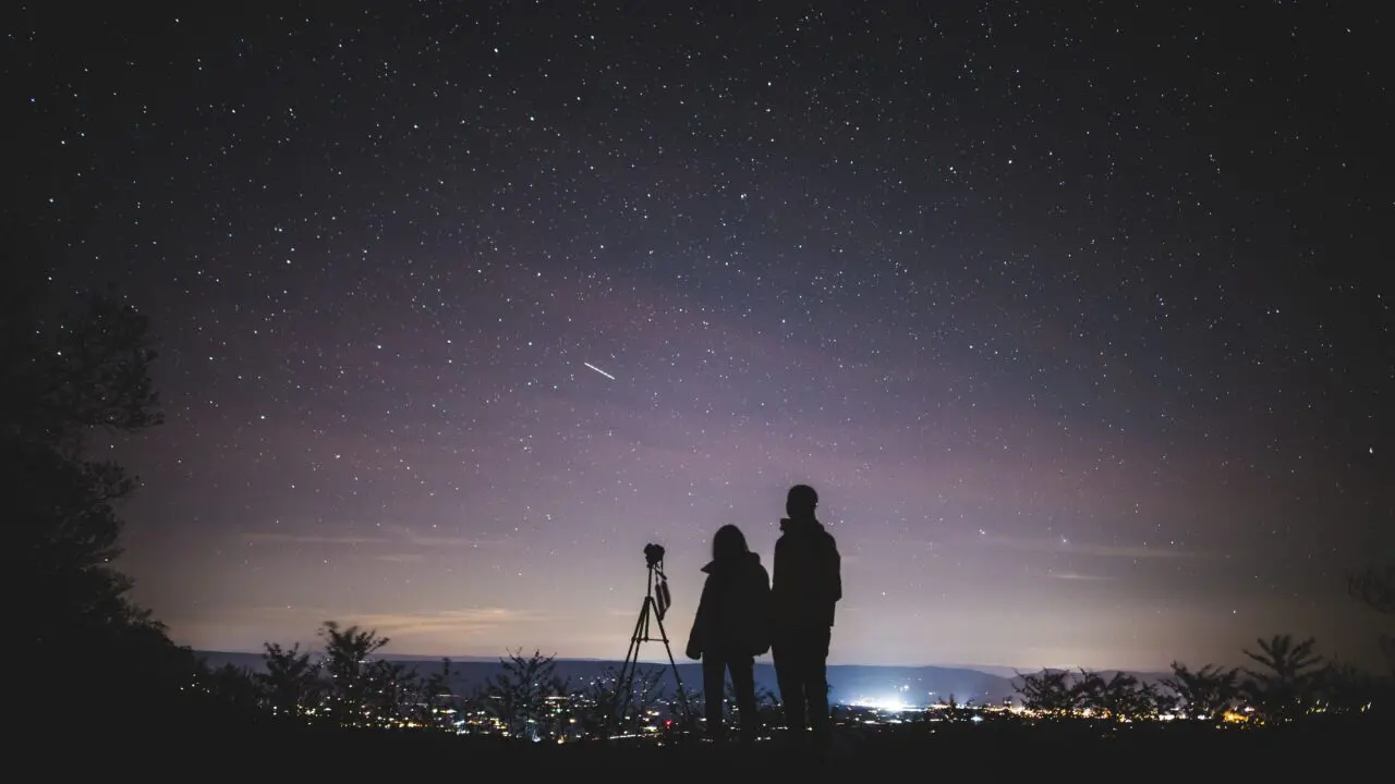Sylwetki dwóch osób obserwujących rozgwieżdżone nocne niebo podczas roju meteorów