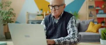 Starszy mężczyzna pracujący przy laptopie w domowym biurze