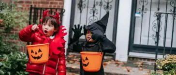 Dzieci w kostiumach diabełka i czarownicy z koszykami w kształcie dyni na Halloween