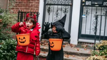 Dzieci w kostiumach diabełka i czarownicy z koszykami w kształcie dyni na Halloween