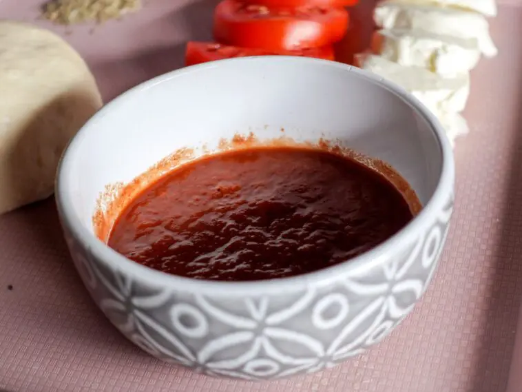 Miska sosu pomidorowego obok świeżych pomidorów i mozzarelli