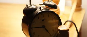 Świecący budzik w ciemności obok łóżka, symbol rozregulowanego rytmu dobowego przy pracy na nocne zmiany
