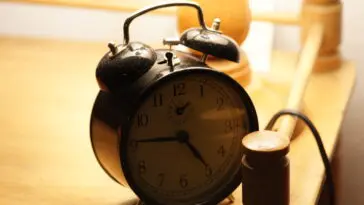 Świecący budzik w ciemności obok łóżka, symbol rozregulowanego rytmu dobowego przy pracy na nocne zmiany