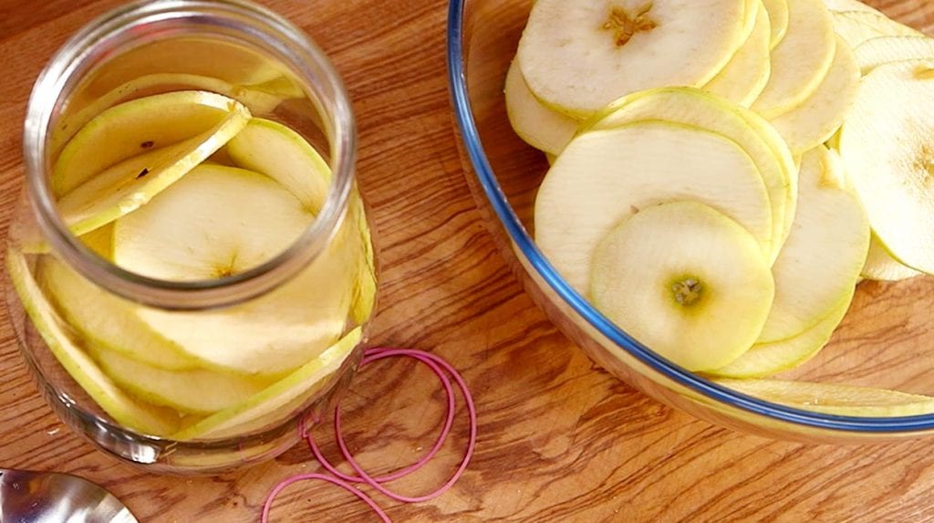 Jabłko, pokrojone na talarki i umieszczone w słoiku oraz szklanej misie. 