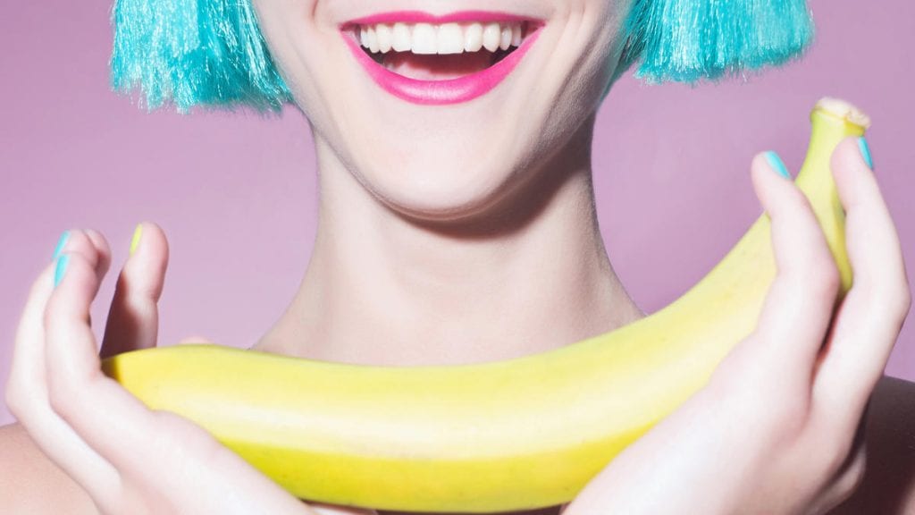 Uśmiechnięta kobieta, trzymająca w dłoni banana. 