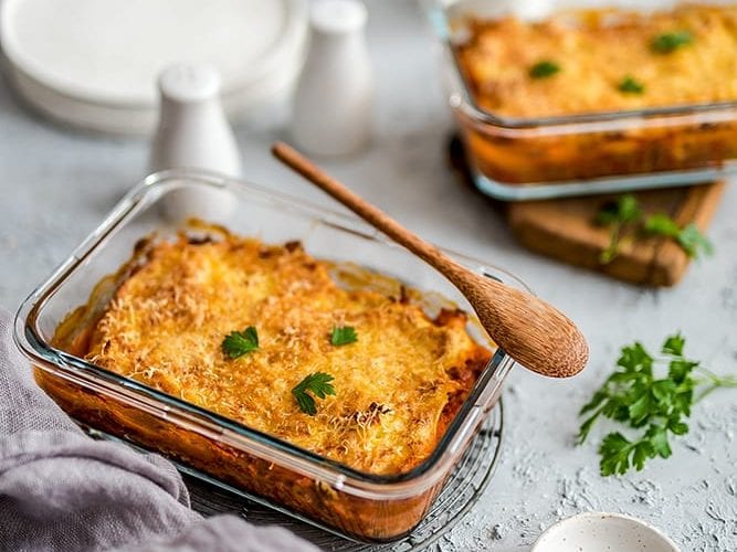 Top 5 przepisy na zapiekanki, czyli smaczny obiad w pół godziny Naczynie żaroodporne, w którym znajduje się zapiekanka. Na nim znajduje się drewniana łyżka.