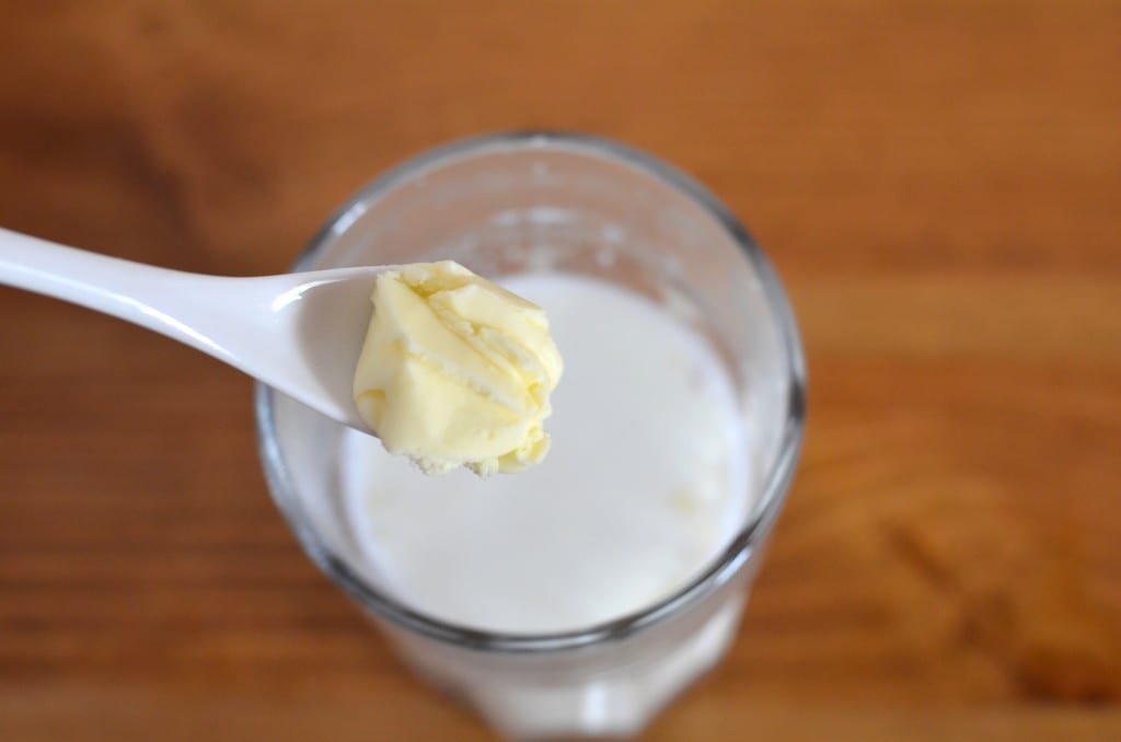 Masło na łyżeczce nad szklanką mleka. 