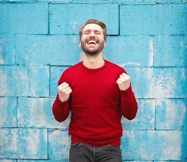 Uśmiechnięty mężczyzna w czerwonym swetrze na tle niebieskiej ściany. 