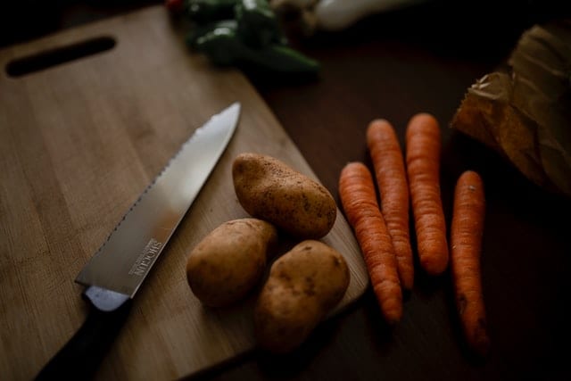 Nóż, ziemniaki i marchew na desce do krojenia.