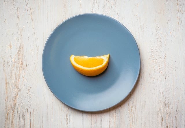 Błękitny talerz, na którym jest kawałek pomarańczy. 
