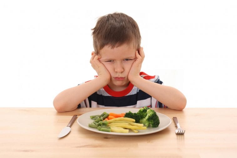 Rozzłoszczone dziecko nad talerzem z jedzeniem.
