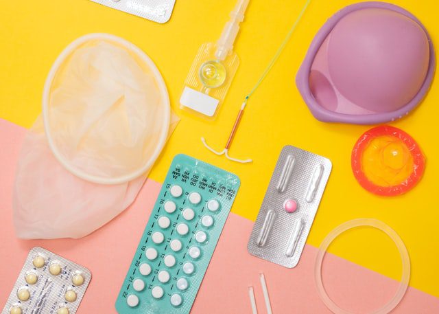 Tabletki antykoncepcyjne i prezerwatywy na kolorowym tle.
