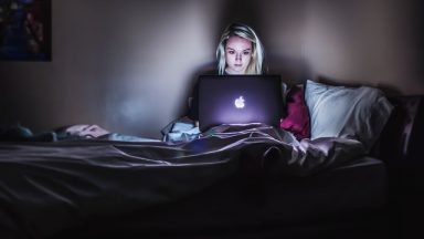 Młoda dziewczyna siedząca nocą na łóżku przed komputerem.