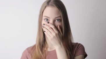 Młoda kobieta zasłania usta dłonią, wstydząc się nieświeżego oddechu