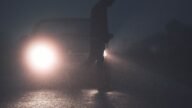 Sylwetka pieszego na drodze oświetlona reflektorami samochodu po zmroku
