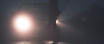 Sylwetka pieszego na drodze oświetlona reflektorami samochodu po zmroku