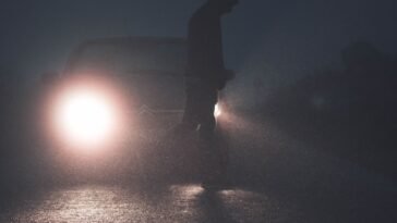 Sylwetka pieszego na drodze oświetlona reflektorami samochodu po zmroku