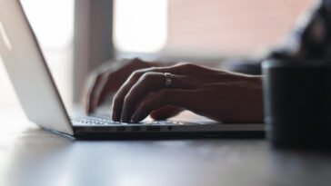 Dłonie piszące na klawiaturze laptopa, praca przy komputerze a ryzyko zespołu cieśni nadgarstka