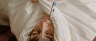 Chory mężczyzna leżący w łóżku pod kocem z termometrem, zwolnienie lekarskie