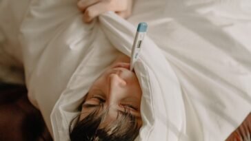 Chory mężczyzna leżący w łóżku pod kocem z termometrem, zwolnienie lekarskie