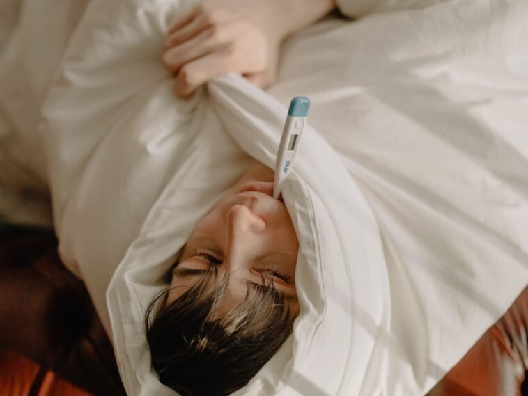 Na zwolnieniu jest cyfra, która mówi, czy wolno ci wyjść z domu. Większość pracowników nigdy na nią nie spojrzała Chory mężczyzna leżący w łóżku pod kocem z termometrem, zwolnienie lekarskie