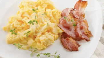 Keto śniadanie: jajecznica z chrupiącym boczkiem i tymiankiem na białym talerzu