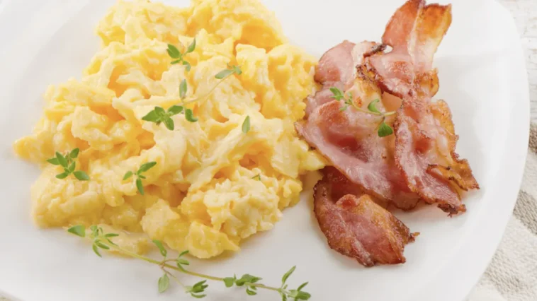 Keto śniadanie: jajecznica z chrupiącym boczkiem i tymiankiem na białym talerzu