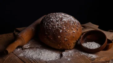 Bochenek chleba z mąką i wałkiem na drewnianym stole, gluten w pieczywie
