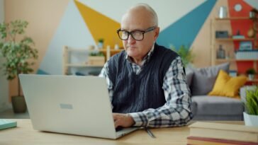 Starszy mężczyzna pracujący przy laptopie w domowym biurze