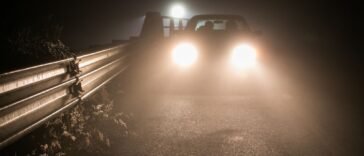 Samochód z włączonymi reflektorami na ciemnej, zamglonej drodze po zmroku