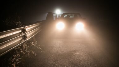 Samochód z włączonymi reflektorami na ciemnej, zamglonej drodze po zmroku