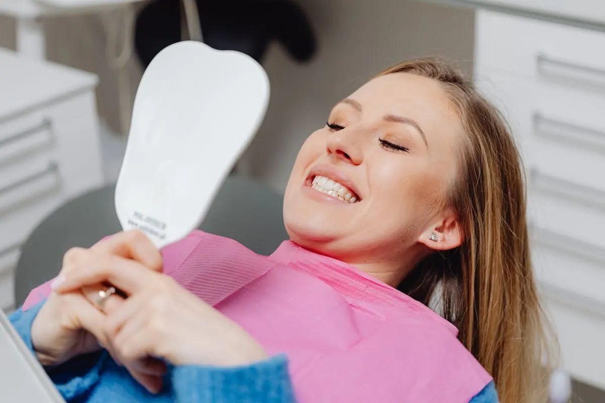 Uśmiechnięta pacjentka ogląda w lusterku zęby po zabiegu u dentysty