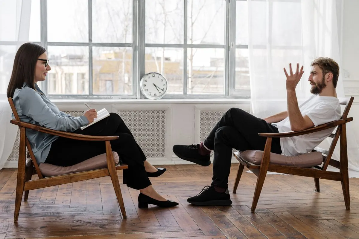 Sesja terapii psychologicznej, psychoterapeutka z notatnikiem rozmawia z mężczyzną w gabinecie